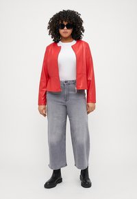 Κόκκινο φανέλα δερμάτινο μπουφάν με φερμουάρ, γκρίζες φαρδές παντελόνες, μαύρες μπότες μέχρι τον αστράγαλο και λευκό μπλουζάκι; μοντέλο με γυαλιά ηλίου.