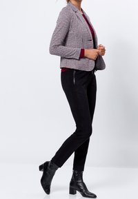 Blazer à carreaux rouge et noir avec une coupe ajustée, associé à un pantalon slim en daim noir et des bottes à talons de longueur cheville.