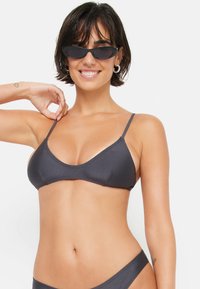 Top bikini grigio scuro con spalline sottili, caratterizzato da una forma triangolare e una texture liscia. Abbinato a occhiali da sole ovali neri.