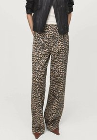 Béžové a čierne nohavice širokého strihu s leopardím vzorom, vyrobené z hladkého materiálu a s vysokým pásom. Doplnené o hnedé špicaté topánky.
