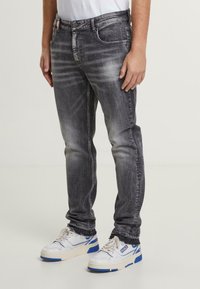 Jeans de mezclilla elásticos negros desteñidos con corte ajustado, que presentan un sutil desgaste, cinco bolsillos y detalles bordados en la cinturilla.