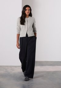 Világosszürke, texturált kardigán környakrésszel és gombos záródással, bő szabású fekete nadrággal és szürke lábbelivel párosítva.