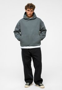 Grijze hoodie met een buidelzak aan de voorkant, gecombineerd met zwarte losse spijkerbroeken en zwarte sneakers. Getextureerde stof met een ontspannen pasvorm.