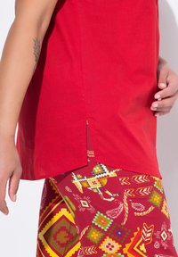 Top in cotone rosso con fessure laterali abbinato a pantaloni rossi a fantasia con design geometrici nei toni di giallo, verde e blu.