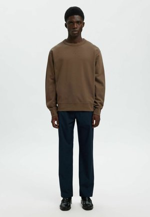 Sweatshirt marron avec un col rond, des manches longues et des poignets côtelés, associé à un pantalon droit bleu marine et des chaussures noires.