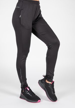 Leggings de sport noirs avec un design fuselé, taille élastique, poches latérales et détails réfléchissants. Portés avec des chaussures noires arborant des accents roses.