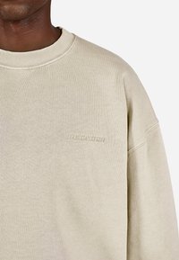 Bežová mikina s ryhovaným okrúhlym výstrihom, vo voľnom strihu a s reliéfnym logom značky na hrudi. Vyrobené z jemnej, textúrovanej tkaniny.