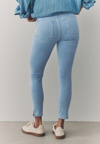Blugi skinny din denim bleu deschis, cu croială strâmtă, două buzunare în spate și crăpături în tiv, asortați cu adidași bej.