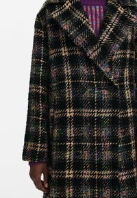 Double-breasted coat in black and beige plaid, featuring colorful woven accents, textured fabric, large lapels, and two buttons.