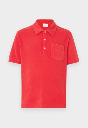 Polo rojo hecho de suave tela de rizo, que presenta un collar clásico, una tapeta con tres botones y un bolsillo parche en el pecho izquierdo.