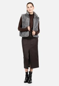 Šedá vesta z umělé kožešiny se zipem vpředu, vrstvená přes hnědé tričko s dlouhým rukávem. Hnědá sukně s předním rozparkem, doplněná černými kotníkovými botami.