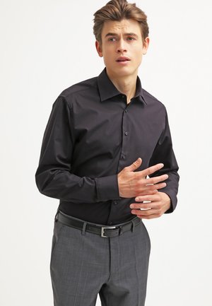 Camicia nera a maniche lunghe con colletto classico e chiusura a bottoni, abbinata a pantaloni a quadri grigi e una cintura nera. Tessuto liscio.