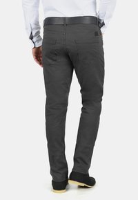 Pantalon chino en coton gris, coupe slim, avec poches arrière et ceinture noire, assorti à des bottines noires, sur un fond clair.
