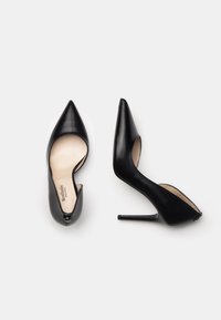Chaussures à talons hauts en cuir noir avec un bout pointu et des côtés découpés, présentant un design élégant et un talon aiguille. Détail avant discret.