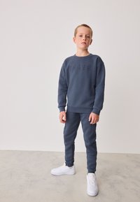 Dunkelblauer Pullover mit reliefartigem "BAKER"-Schriftzug, kombiniert mit passenden Jogginghosen. Verfügt über gerippte Bündchen und Seitennähendetails. Weiße Sneaker.