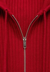 Pull rouge côtelé avec une fermeture éclair argentée, doté d'une capuche et de cordons, mettant en valeur un tissu texturé et des rainures horizontales.