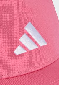 Gorra rosa hecha de algodón con una textura suave y un logo de tres franjas bordado en blanco en la parte delantera.