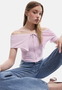 Lyserød ribbet off-the-shoulder top med korte ærmer og lynlås foran, parret med lyseblå denim jeans med subtile glimmer.