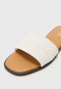 Witte geweven slider sandaal met een brede band, voorzien van een gladde tan voetbed en een zwarte buitenzool. Textuur materiaal met matte afwerking.
