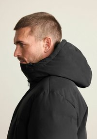 Schwarze isolierte Steppjacke mit hohem Kragen und verstellbarer Kapuze. Glatte Textur mit durchgehendem Reißverschluss vorne und ohne sichtbare Muster.