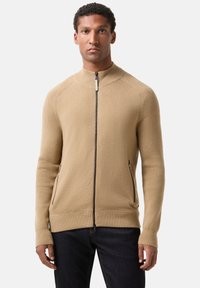 Beiger Reißverschluss-Pullover aus strukturiertem Stoff mit gerippten Akzenten, hohem Kragen und zwei Seitentaschen mit Reißverschluss.