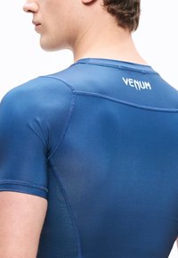 Μπλε μπλουζάκι συμπίεσης κατασκευασμένο από ελαφρύ, ελαστικό υλικό. Διαθέτει κοντά μανίκια, επίπεδα ραφές και λευκό λογότυπο "VENUM" στην πλάτη.