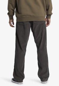 Tmavě šedé manšestrové kalhoty s volným střihem, s dvěma zadními kapsami a texturovaným povrchem. Nošeny s černobílými teniskami.