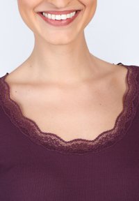 Lila gerippter Oberteil mit einem gewellten Spitzen-Ausschnitt. Der Stoff wirkt weich, mit einer reichen Textur und Detailarbeit im Spitzenbesatz.