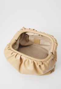 Beige nahkastu kott, millel on volditud disain, varustatud tõmbluku sulgemisega ning voodriga sisemus, millel on peen herringbone muster.