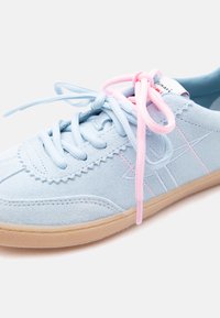 Baskets en daim bleu clair avec semelle en gomme, lacets bleus et roses noués en nœud, présentant des motifs cousus et un design décontracté.