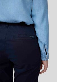 Chemise bleu clair à manches longues, en tissu texturé ; associée à un pantalon noir marine avec une poche arrière et un petit logo.
