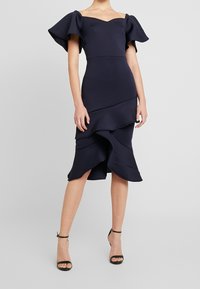 Mörkblå off-shoulder klänning med volangiga korta ärmar och lager-på-lager nederdel. Tillverkad av strukturerad tyg, med en åtsittande byst.