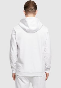 Felpa bianca con design a pullover, realizzata in tessuto morbido. Presenta un grande cappuccio e polsini a costine, con una vestibilità rilassata.