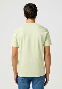 Ljusgrön t-shirt med kort ärm och rund halsringning, slät textur och figurnära passform, bärs med blå jeans.