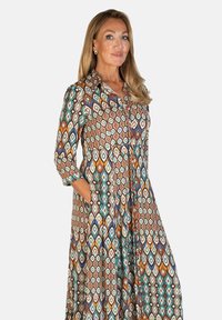 Długa, button-up sukienka z wielokolorowym wzorem geometrycznym w Ziemnych odcieniach. Posiada kołnierzyk, rękawy długości 3/4 oraz boczne kieszenie.