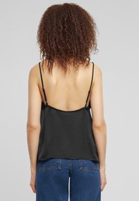 Camisola nera con sottili spalline regolabili, tessuto liscio e vestibilità ampia, caratterizzata da un design con schiena aperta e un leggero lucido.