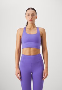 Μωβ αθλητικό crop top με φαρδιές τιράντες και τετράγωνη λαιμόκοψη, συνδυασμένο με ψηλόμεσες κολάν σε ταιριαστό χρώμα, όλα σε μαλακό, ελαστικό ύφασμα.