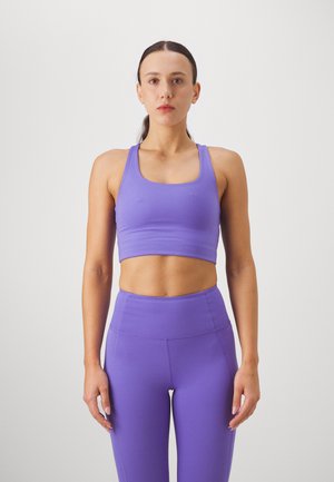 Ljubičasti atletski crop top s širokim naramenicama i četvrtastim dekolteom, u kombinaciji s visokim tajicama u istoj boji, sve od glatkog, rastezljivog materijala.