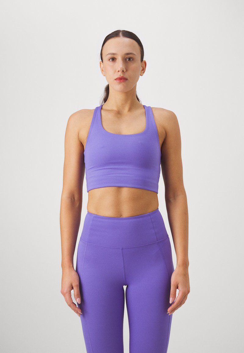 Μωβ αθλητικό crop top με φαρδιές τιράντες και τετράγωνη λαιμόκοψη, συνδυασμένο με ψηλόμεσες κολάν σε ταιριαστό χρώμα, όλα σε μαλακό, ελαστικό ύφασμα.