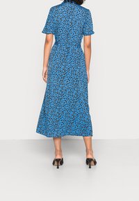 Niebieska sukienka midi w panterkę z krótkimi rękawami, ściągniętym w pasie, z luźną spódnicą, zestawiona z czarnymi, wysokimi klapkami.