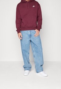 Sudadera con capucha burdeos de Nike con bolsillo delantero, combinada con unos vaqueros de mezclilla holgados azul claro y zapatillas blancas. Material de algodón, diseño casual.