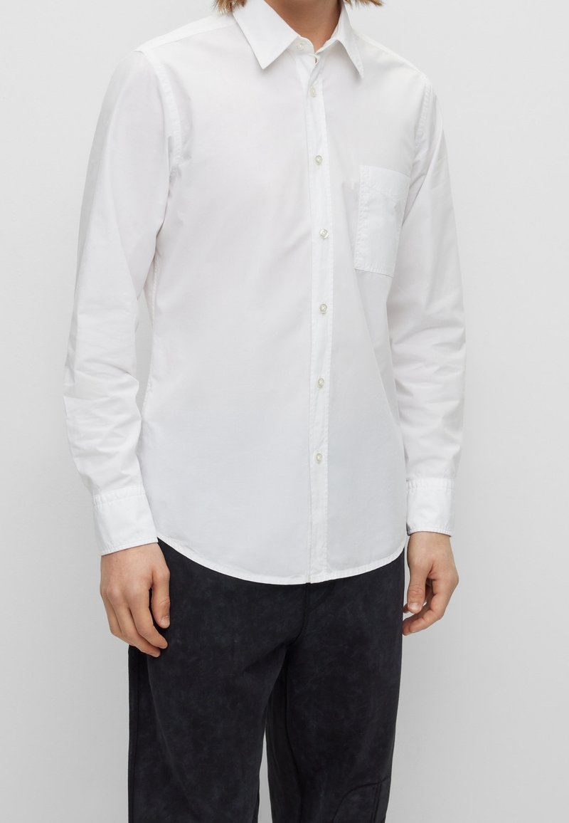 Vit långärmad skjorta med knäppning och spetsig krage, med vänster bröstficka, tillverkad av ett mjukt tyg och med rundad fåll.