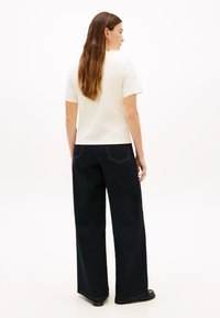 Κρεμ κοντομάνικη μπλούζα συνδυασμένη με σκούρο τζιν φαρδιάς γραμμής. Η μπλούζα έχει στρογγυλή λαιμόκοψη· το τζιν διαθέτει ορατές πίσω τσέπες και ραφές.