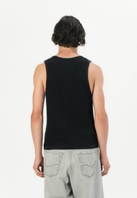 Mustassa ribbatussa tanktopissa on leveät kainalot ja pyöreä pääntie. Helman yksityiskohtainen ompelu yhdistettynä vaaleanharmaisiin farkkuihin.