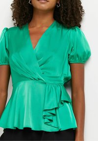 Teal sidentopp med puffärmar, omslagdesign och volangdetalj vid midjan. Slät textur och en figursydd silhuett.