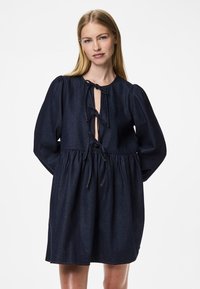 Vestido de ganga azul-escuro com decote redondo, mangas bufantes e um detalhe de laço no corpete. Apresenta um corte solto e uma cintura franzida.