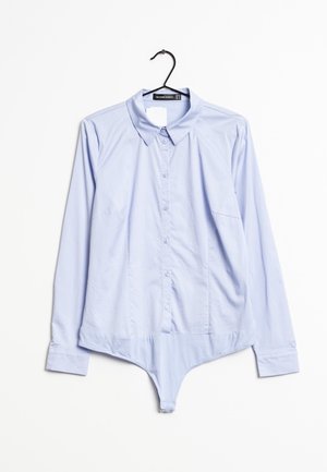 Světle modré body s knoflíkovou dlouhou rukávovou košilí zavěšené na černém ramínku na bílém pozadí.