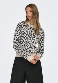 Kreemjas-mustade leopardimustriga pullover ümmarguse kaelusega, soonikkoes varruka- ja alläärtega, valmistatud pehmest tekstuuriga kangast. Sobitatud tumedate pükstega.