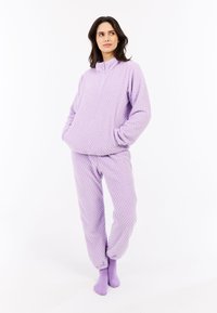 Paarse fleeceloungewear set met een textuur, bestaande uit een half-rits pullover en elastische boorden op de broeken. Zacht en comfortabel ontwerp.