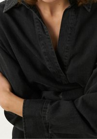 Czarna koszula dżinsowa z kołnierzykiem i szerokimi mankietami, z placketem bez guzików i luźnym krojem. Miękka tekstura i minimalistyczny design.